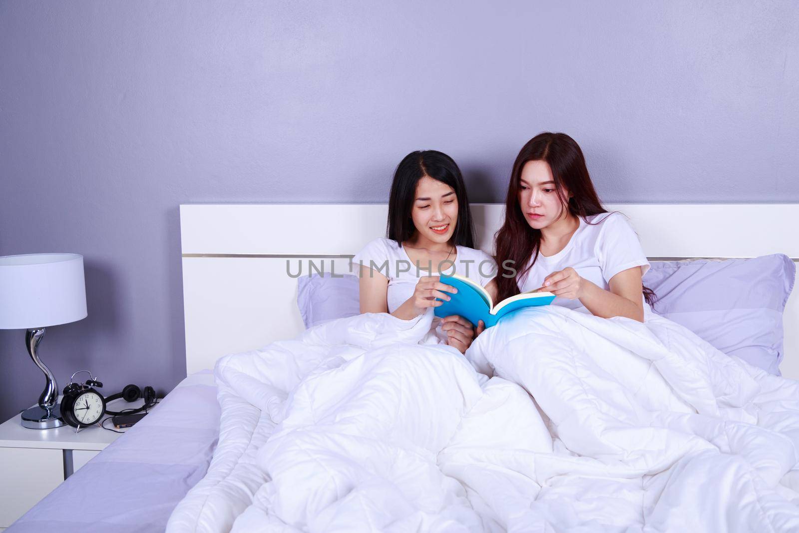 two woman reading a book on bed in the bedroom