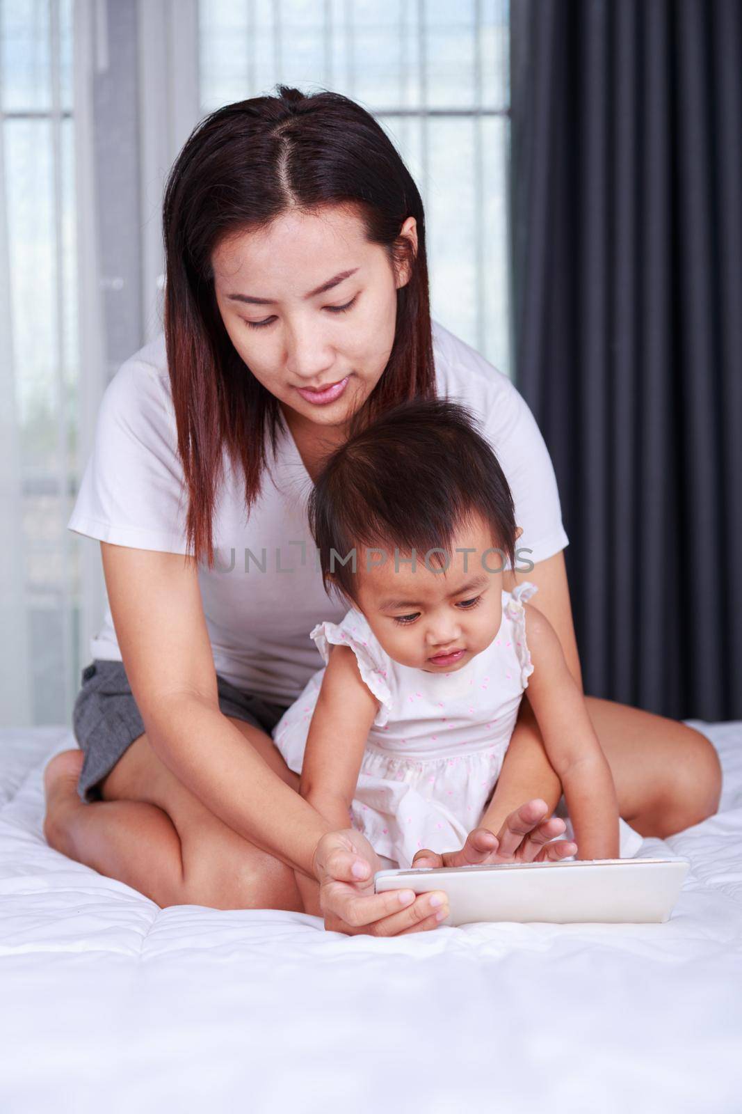 Mother and baby are looking to play and read tablet computer on bed at home