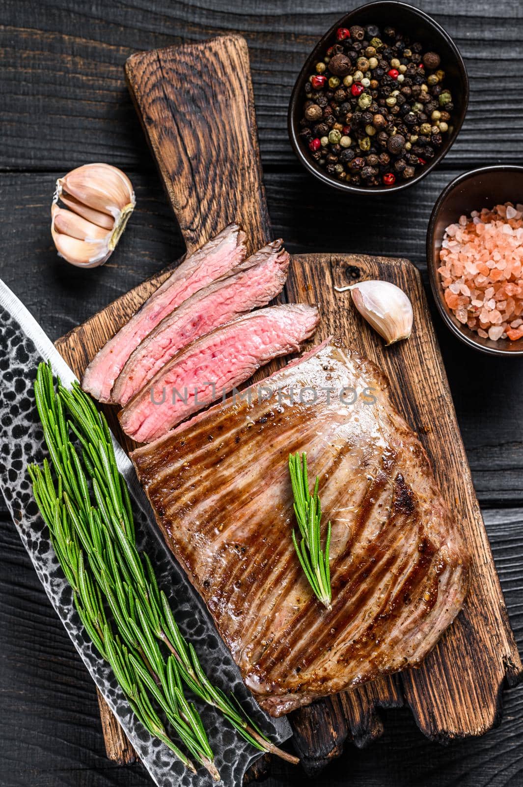 BBQ Grilled flank or flap beef meat steak on a wooden cutting board. Black wooden background. Top view.