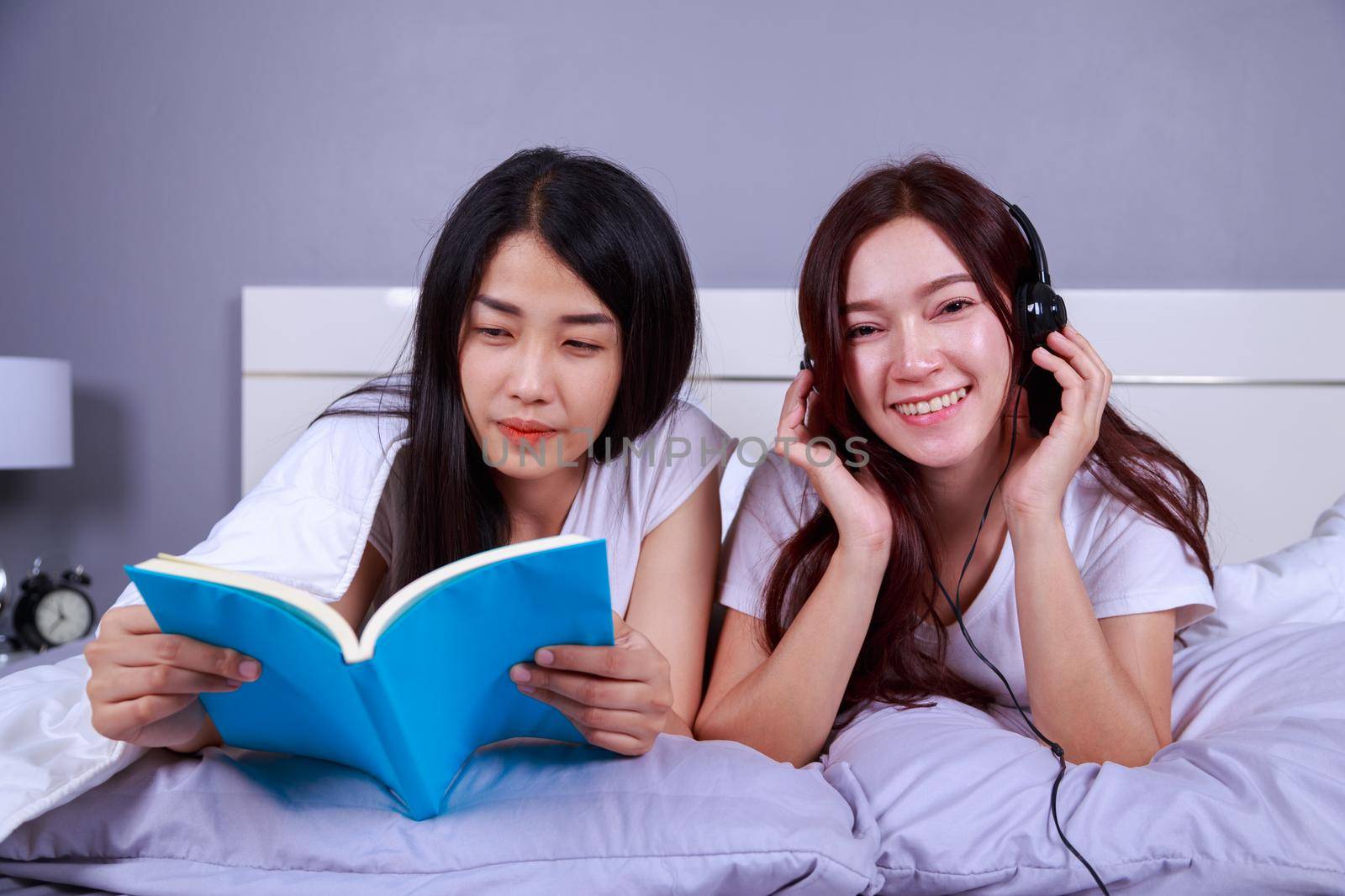 two woman reading a book and using smart phone on bed in the bedroom