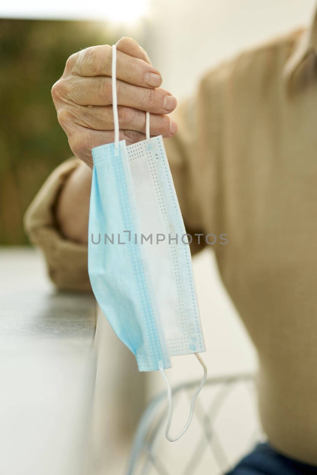 Cropped photo of person holding a surgical mask by the loop