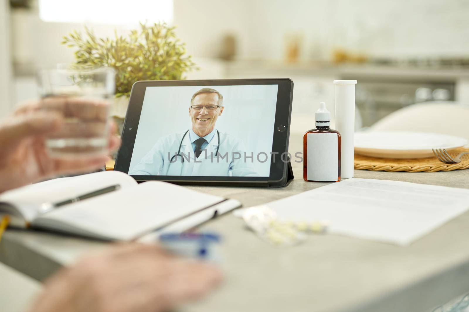 Black tablet with image of a medical worker smiling while video-calling his eldelry patient