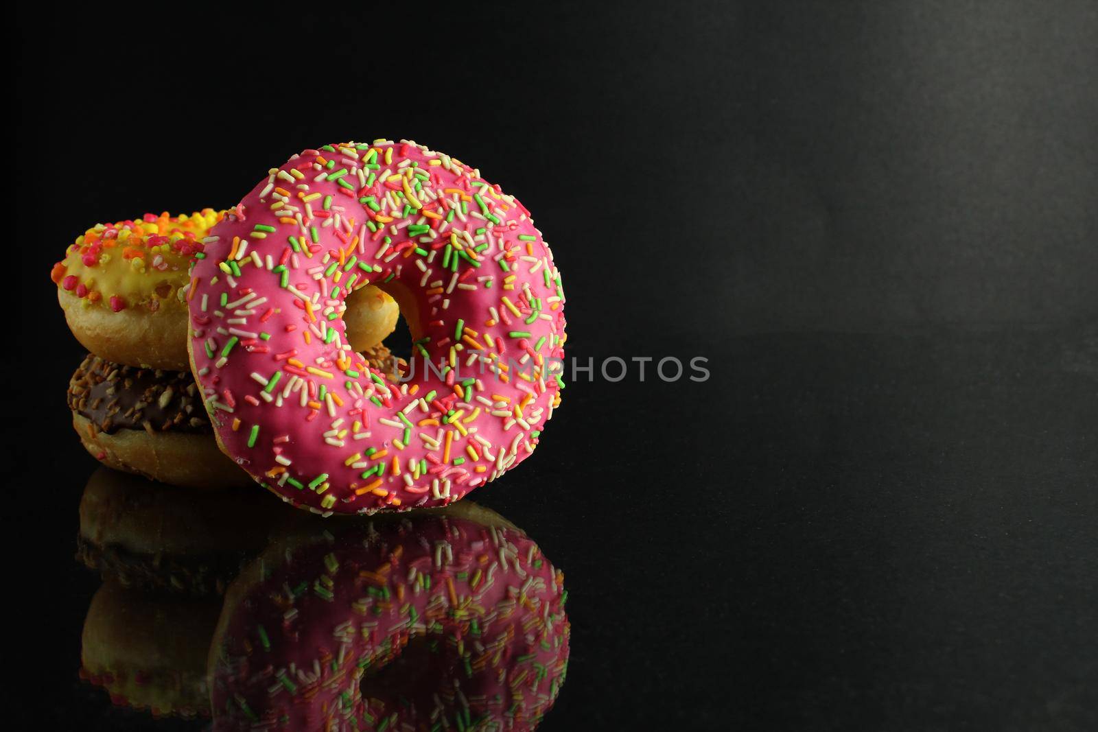 Donuts with icing lie stops and pink bright stands on a black background with room for text.