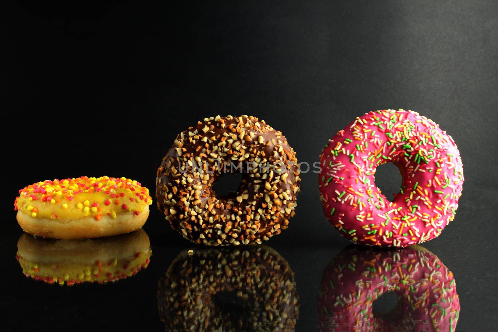 Donuts with icing lie stops and pink bright stands on a black background with room for text.