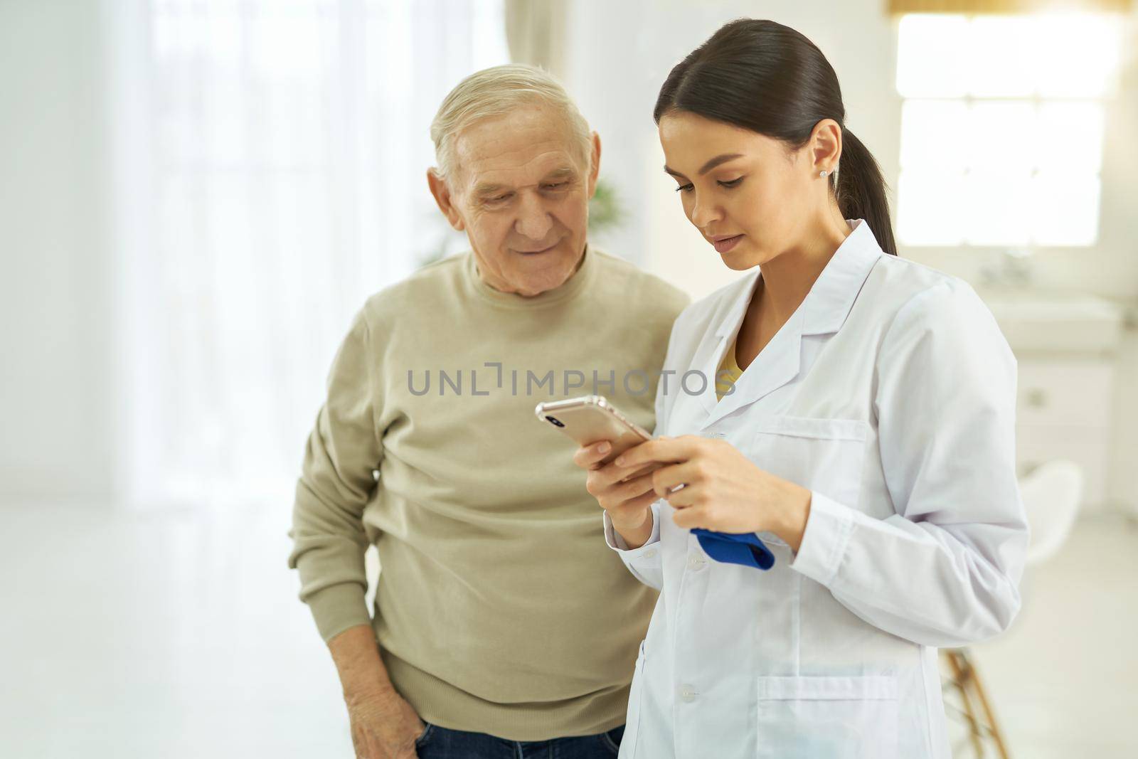 Nurse and elderly man reading messages on mobile phone by friendsstock