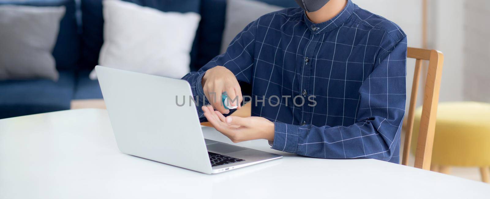 Young asian man work from home with alcohol gel or sanitizer for cleaning hand and protect coronavirus or covid-19, new normal, quarantine and social distancing, businessman using laptop computer. by nnudoo