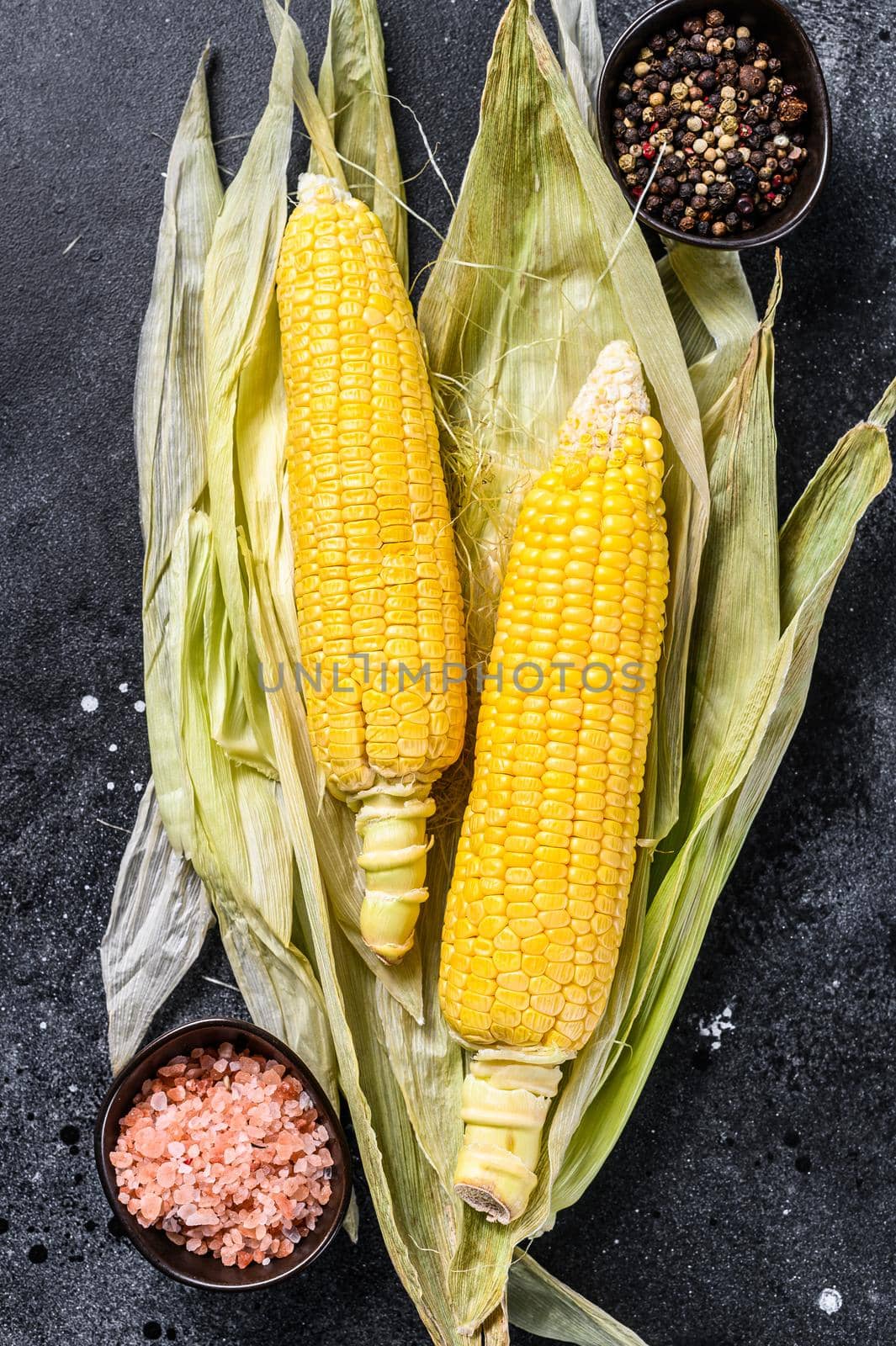 Cooked corn on cobs with salt and pepper. Black background. Top view.