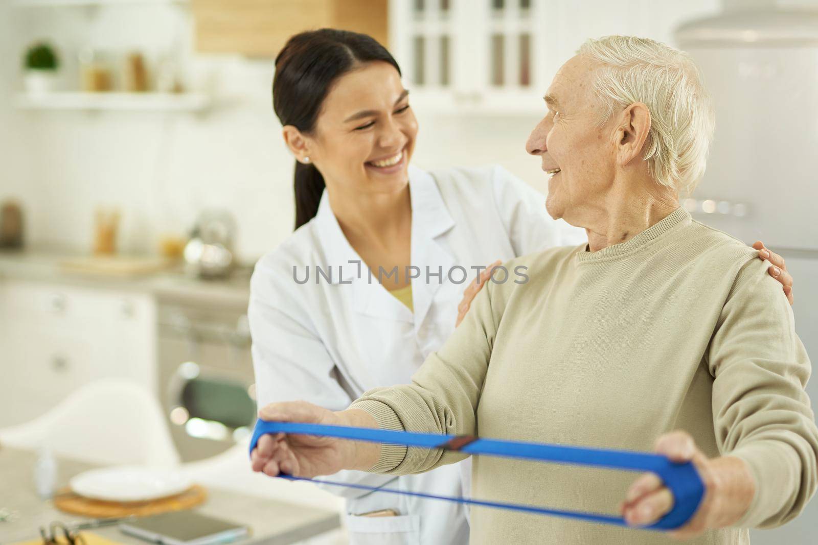 Happy senior citizen doing exercises and holding a fitness elastic band in hands while talking to female doctor