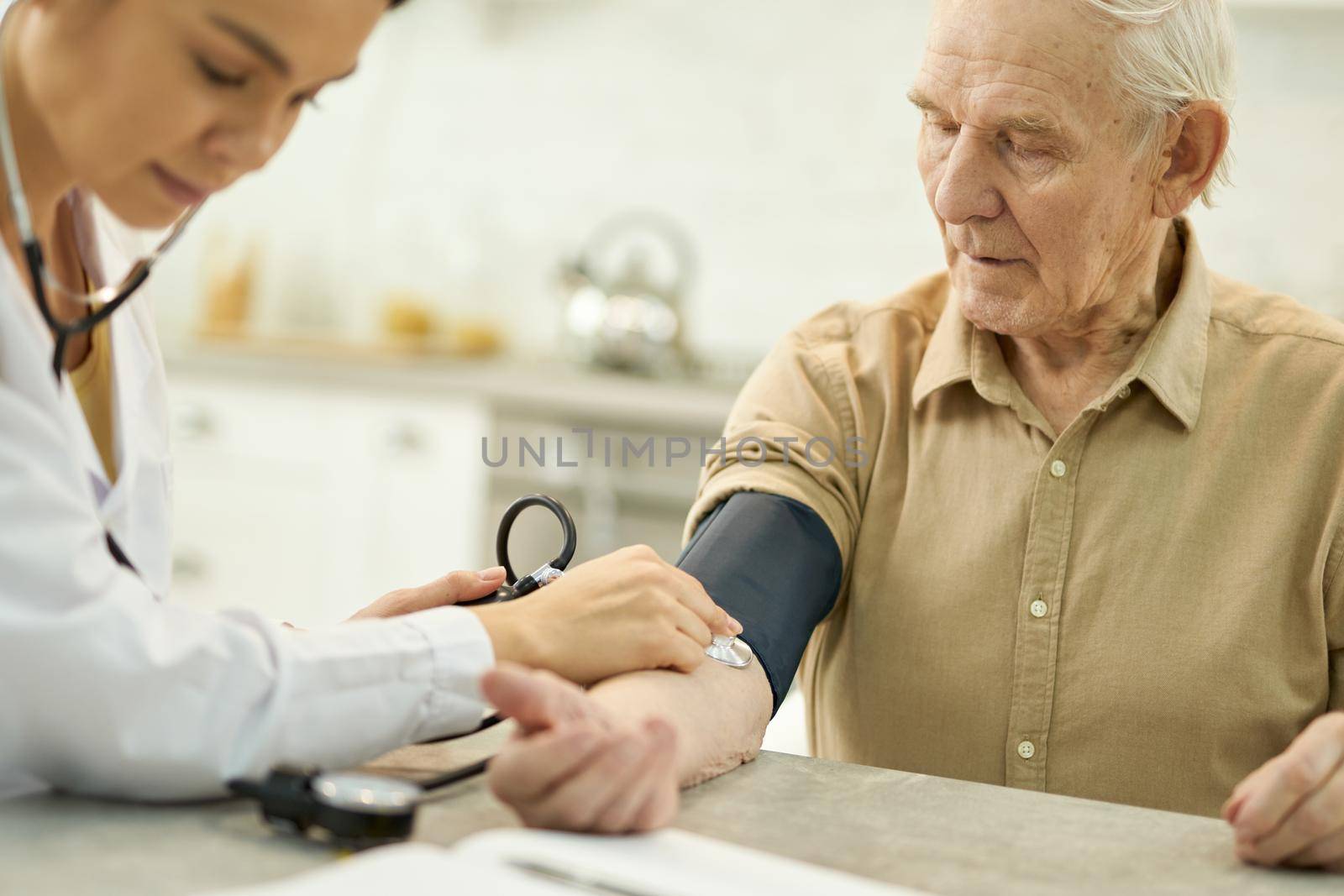 Elderly man with manometer cuff around his upper arm being examined by a young female doctor