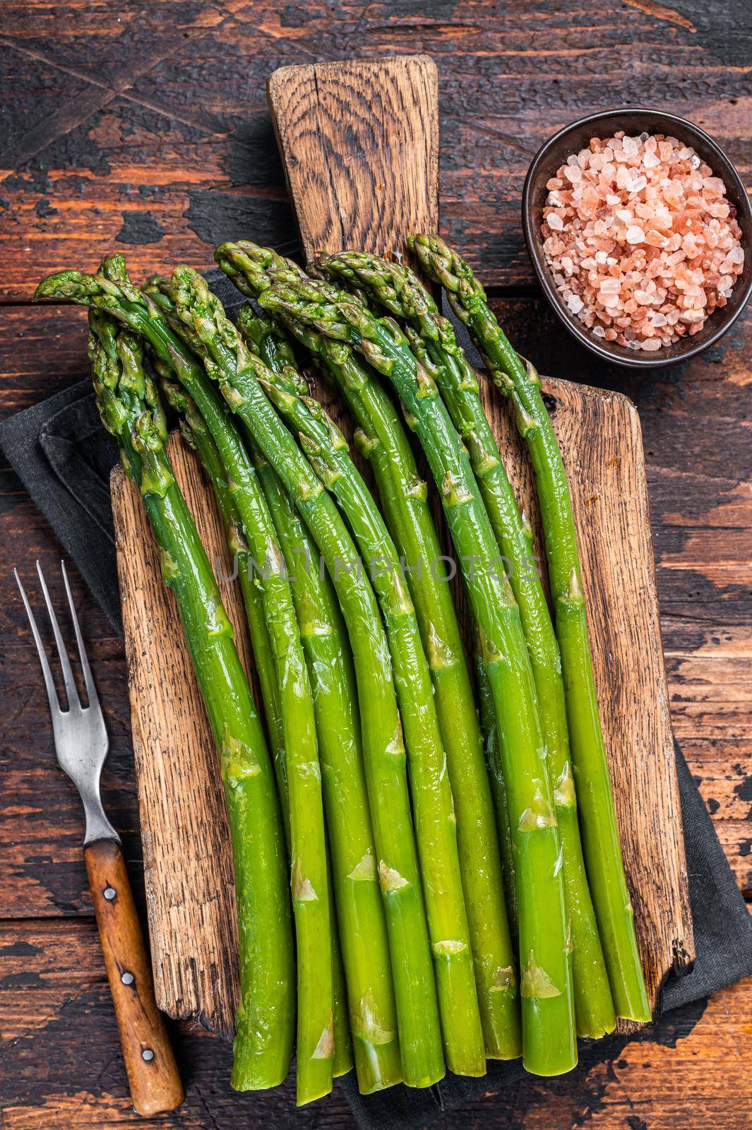 Fresh green asparagus on a wooden cutting board. Dark wooden background. Top view.