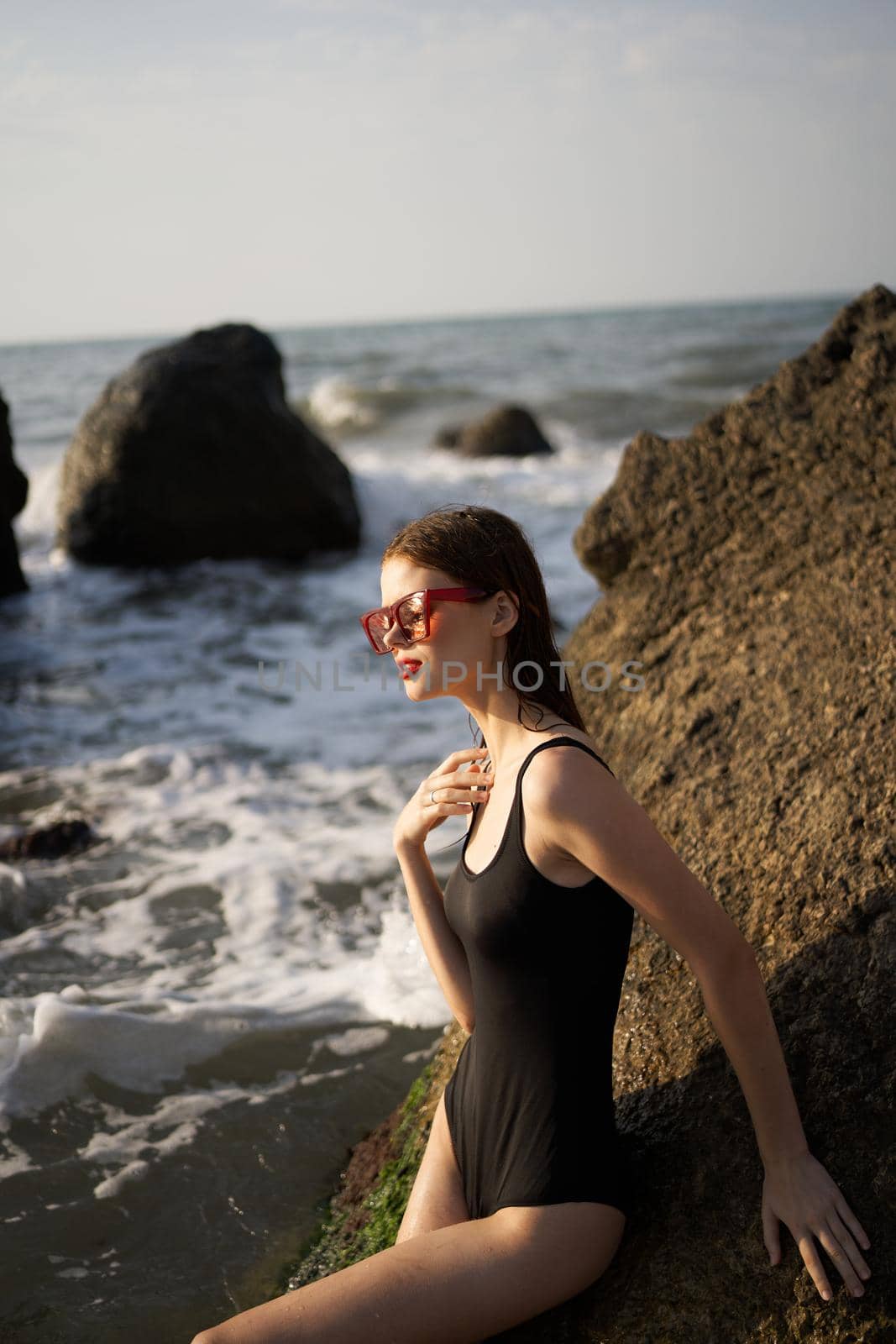 woman in swimsuit sunglasses ocean rocks posing. High quality photo