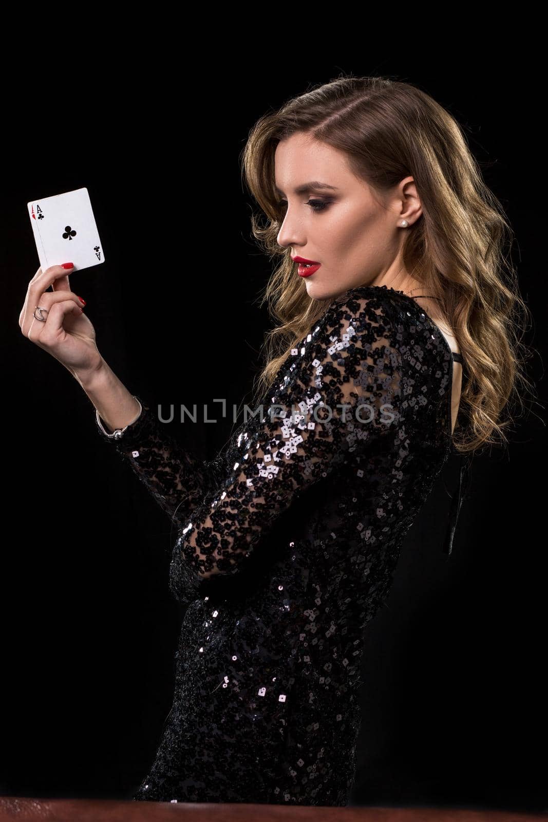 Young beautiful woman in black shiny dress holds poker cards in hands against a black background. The concept of gambling. Casino