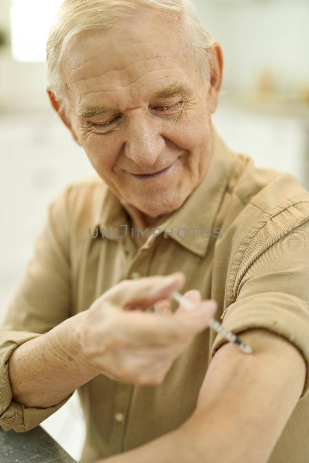 Close-up photo of a mirthful aged man with a rolled-up sleeve performing an arm injection on himself