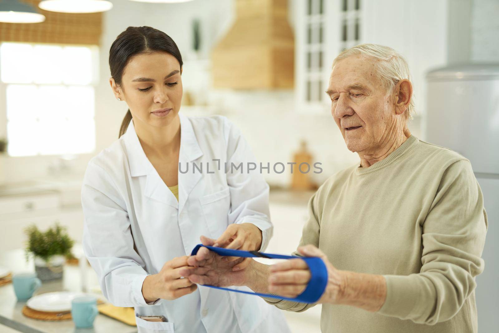 Gray-haired man using fitness rubber band in his apartment by friendsstock