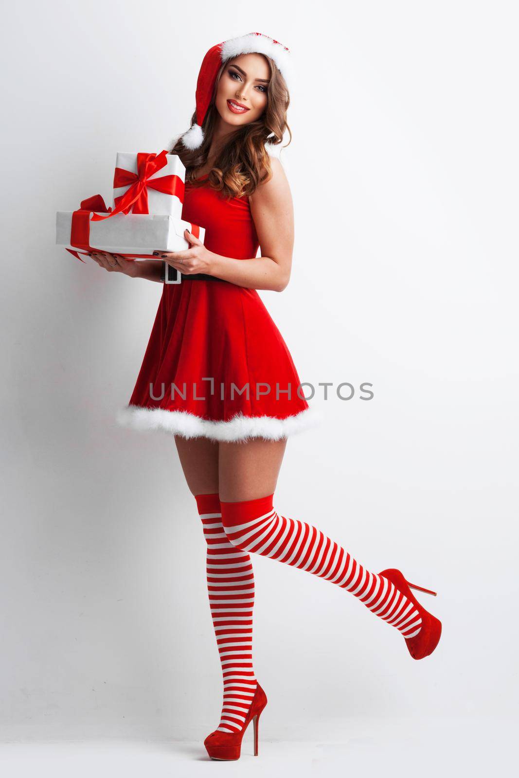 Full length portrait of beautiful girl in Santa Claus style dress and hat holding Christmas gifts