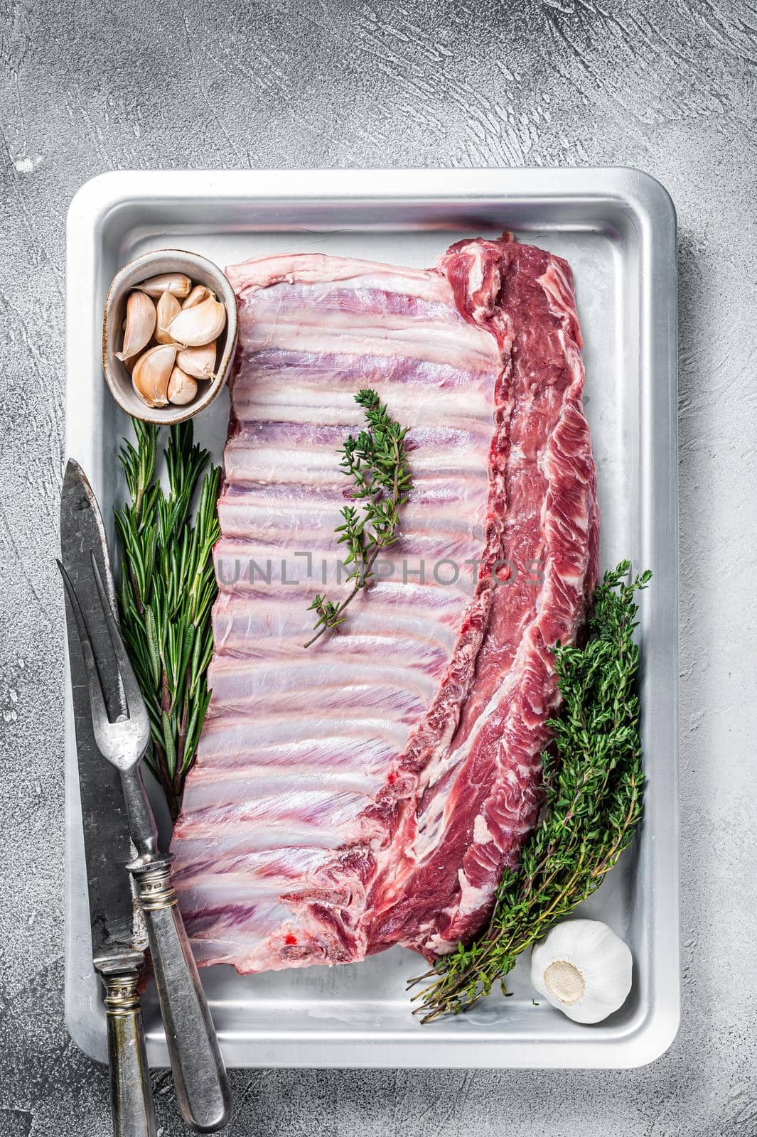 Uncooked raw rack of lamb ribs in baking dish with herbs. White background. Top view.