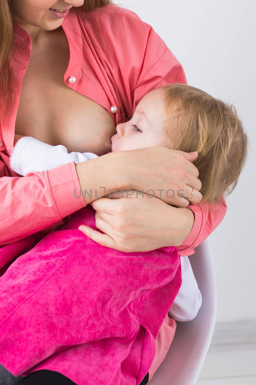 Mother breastfeeding baby in her arms at home. Child eating mother's milk. Young woman nursing and feeding baby. Concept of lactation infant. by Satura86