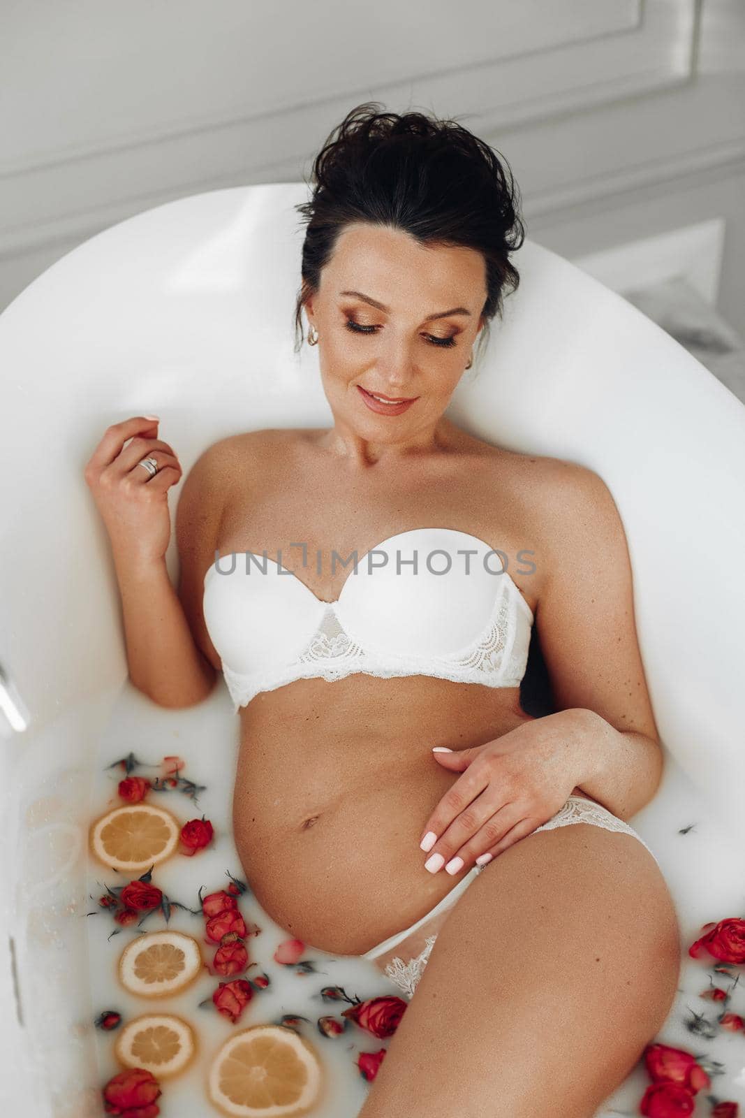 attractive pregnant woman relaxing in the bath with white water and a lot of oranges and flowers by StudioLucky