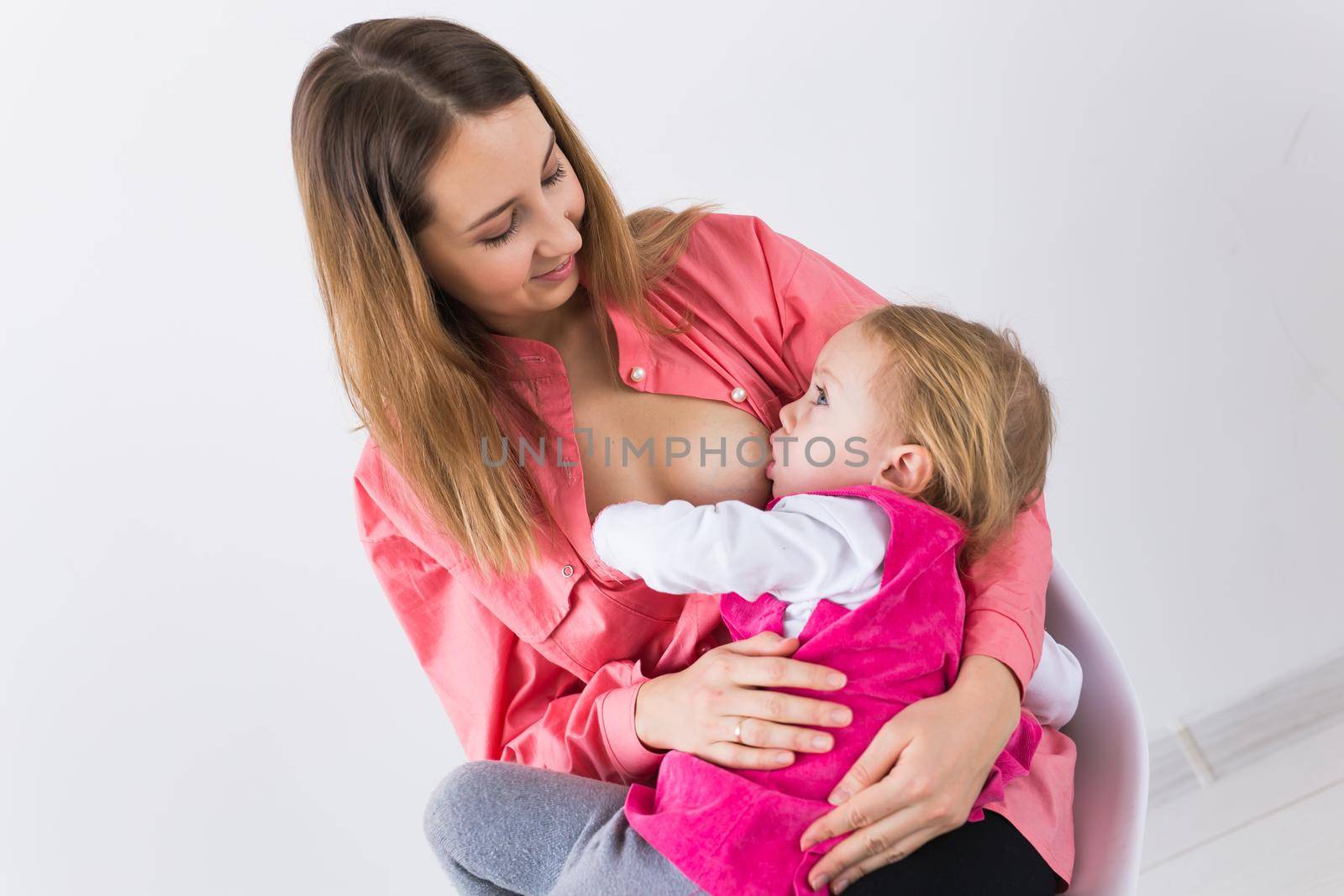 Lactation and motherhood concept - Young beautiful mother holding breastfeeding baby sitting on chair. by Satura86