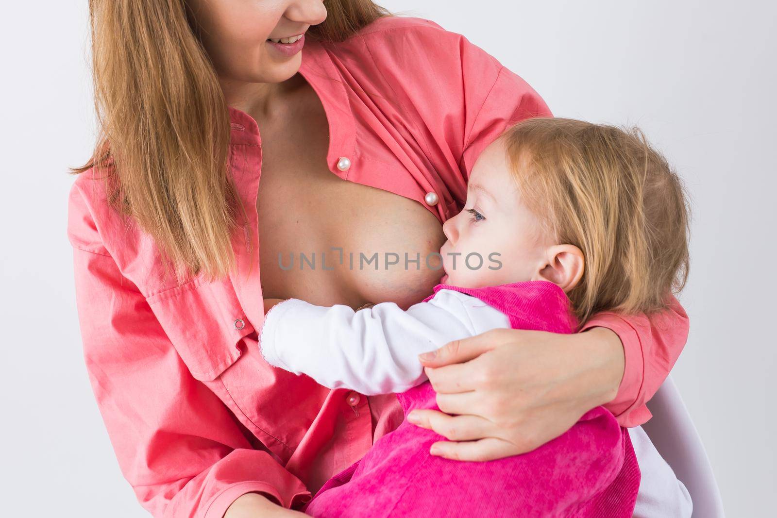 Mother breastfeeding baby in her arms at home. Child eating mother's milk. Young woman nursing and feeding baby. Concept of lactation infant. by Satura86