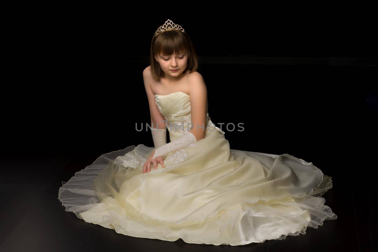 Beautiful little girl sitting in the studio on the floor on a black background. The concept of style and fashion.