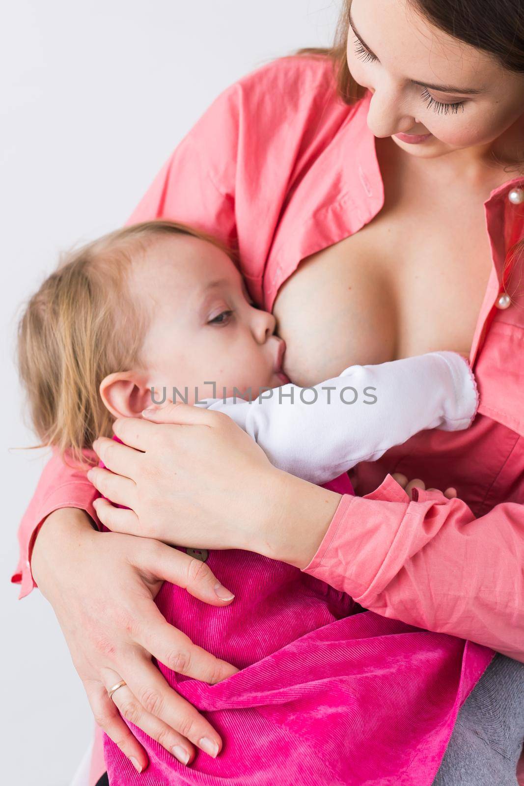 Mother breastfeeding baby in her arms at home. Child eating mother's milk. Young woman nursing and feeding baby. Concept of lactation infant. by Satura86