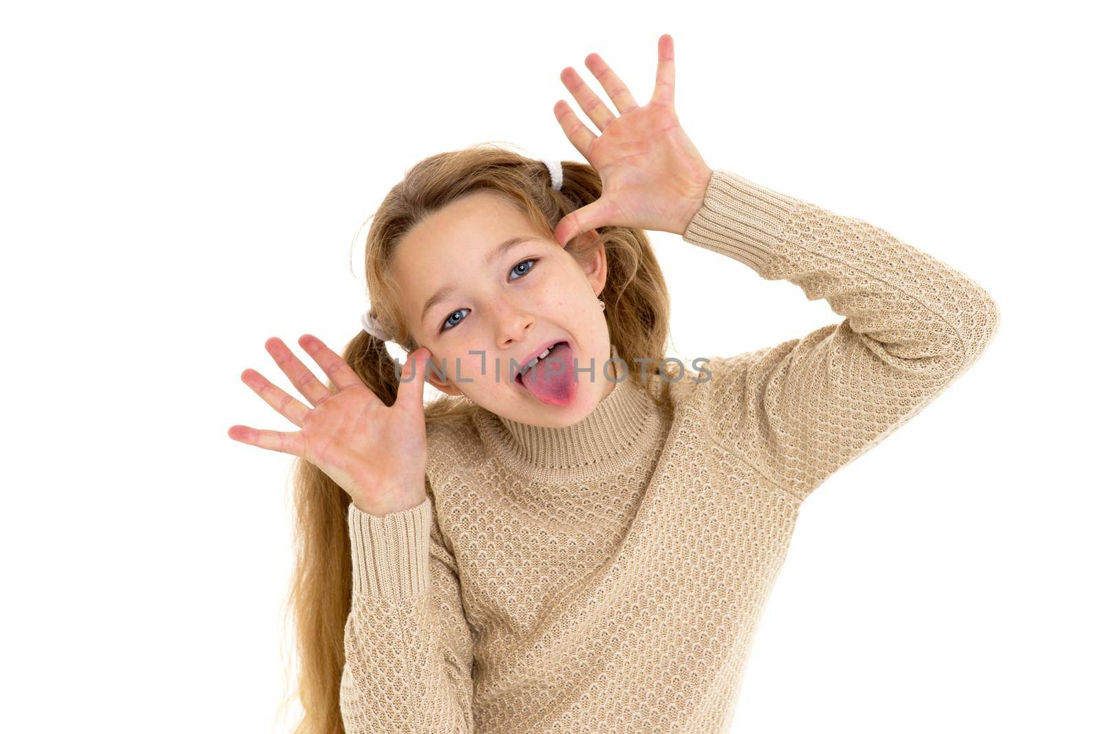 Happy preteen girl showing tongue and gesturing. Funny blonde girl wearing knitted jumper making funny face looking at camera against white background.