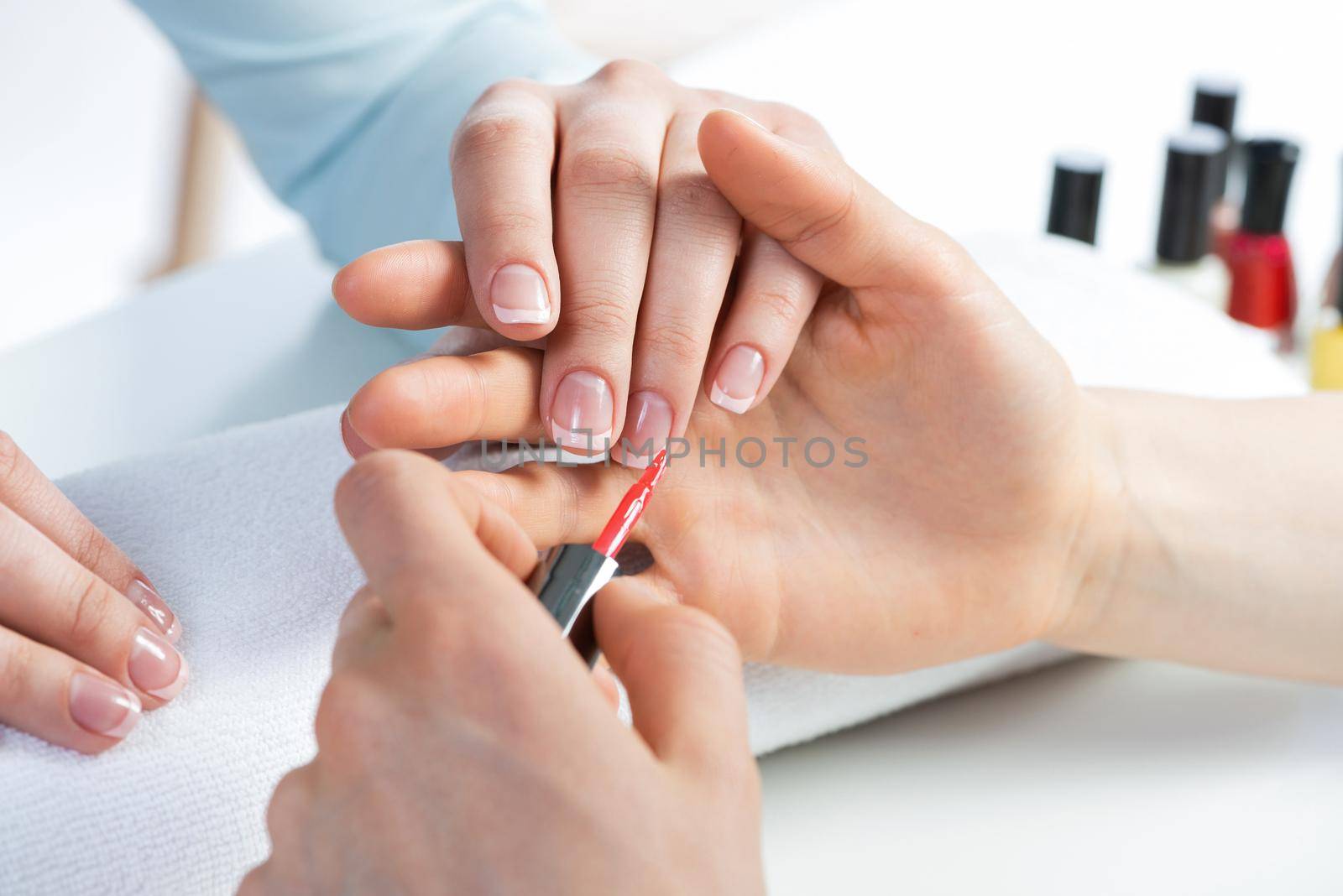 Woman in salon receiving manicure by nail beautician. Professional nail art service advertisement. Closeup of beautiful and groomed female hand applying red nail polish in beauty center.