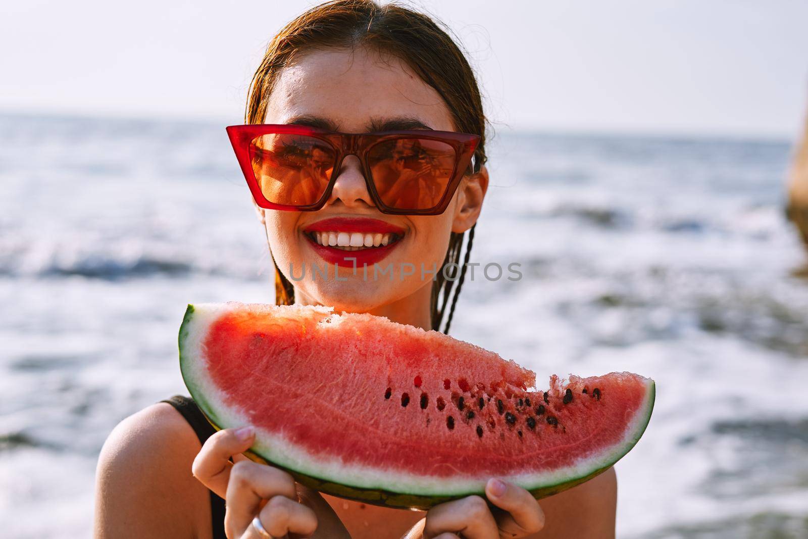 cheerful woman in sunglasses eating watermelon by the ocean. High quality photo