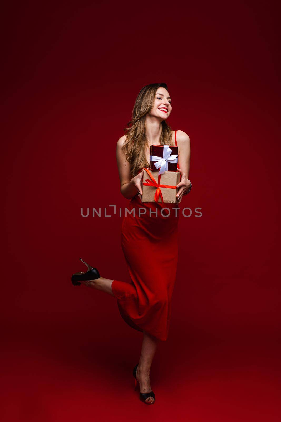 Full length of smiling pretty woman posing and holding gift boxes, isolated on red background. Saint Valentine Day concept