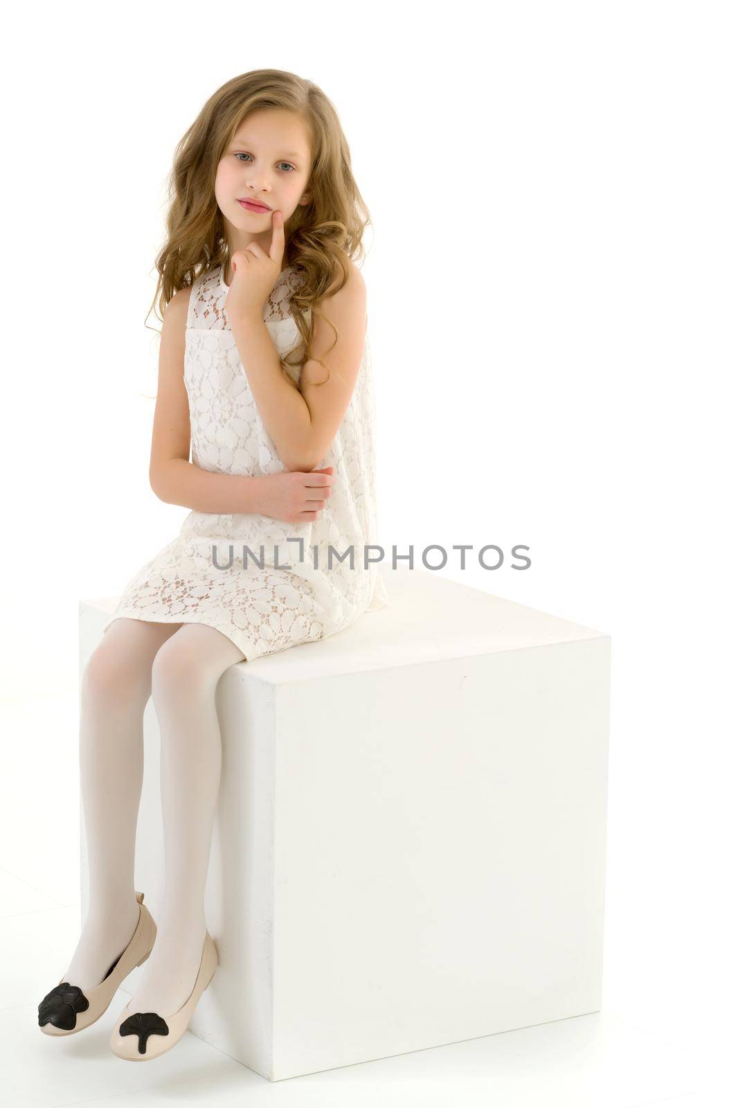 Beautiful Blonde Girl in Elegant Ivory Dress Sitting on White Cube in Studio, Portrait of Cheerful Long Haired Girl Wearing Fashionable Stylish Clothes Posing in Front of Camera Against White Background