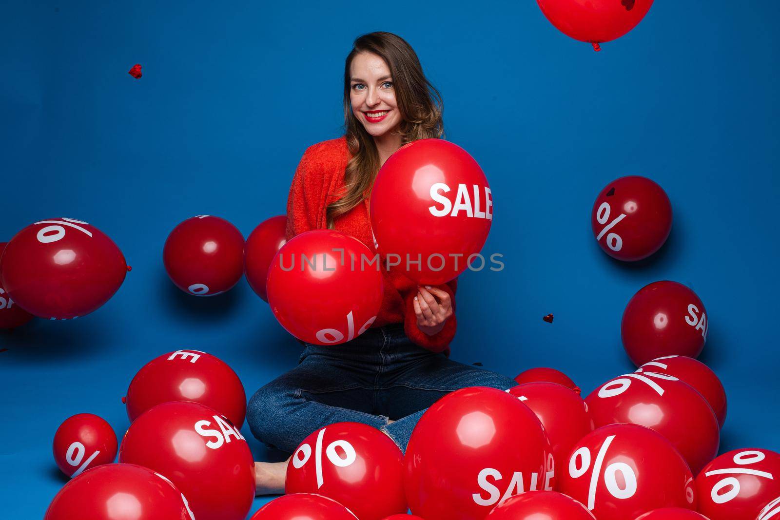 Happy young woman surrounded by balloons with discount stickers by StudioLucky