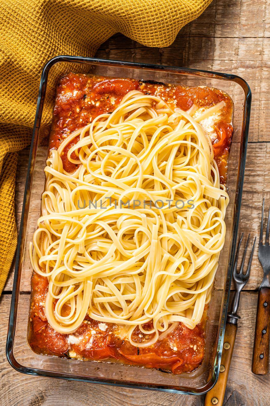 Oven roasted feta pasta with tomatoes in baking dish. Wooden background. Top view.