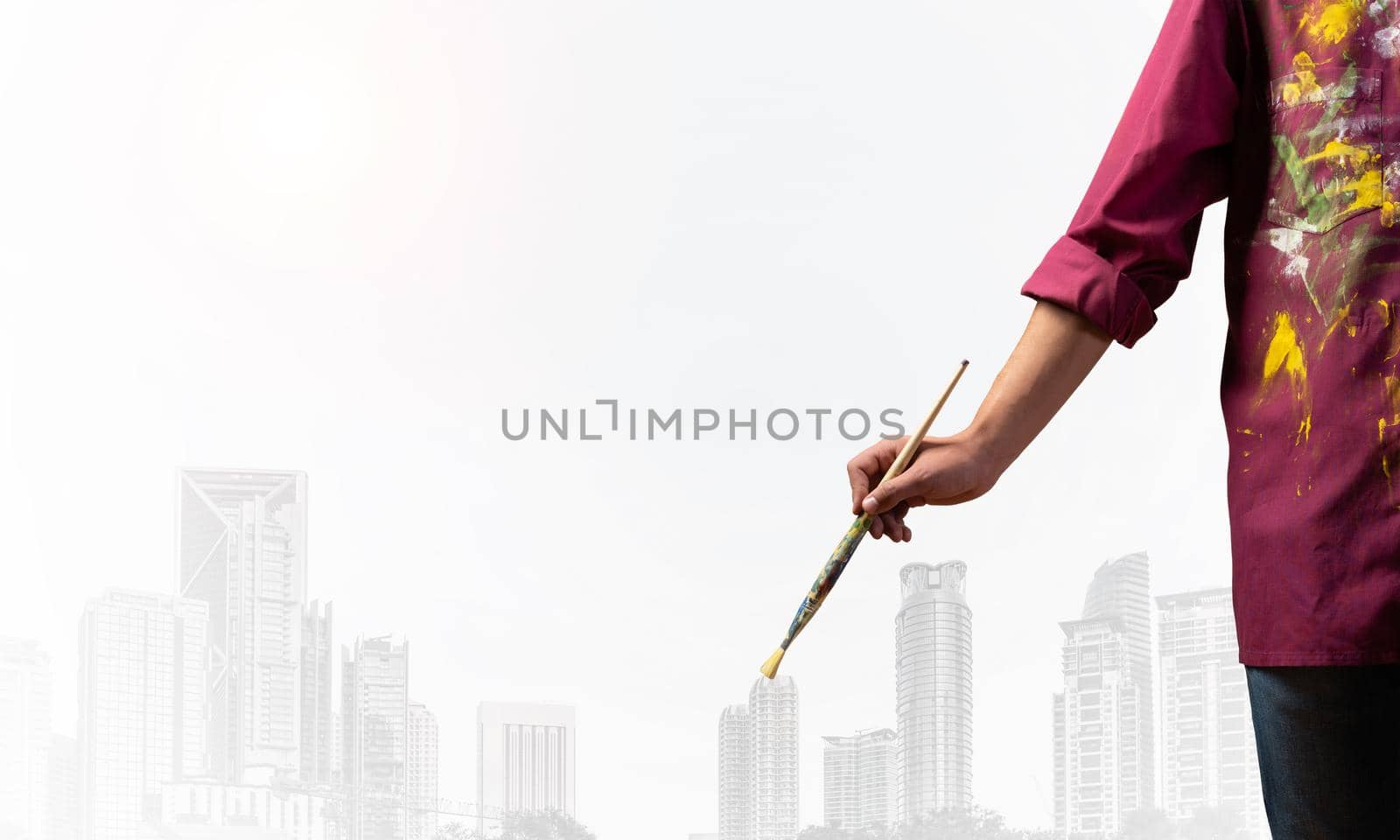 Close up artist hand holding paintbrush. Painter in shirt standing on background modern skyscrapers. Creative hobby and artistic occupation concept with copy space. Art imagination and inspiration