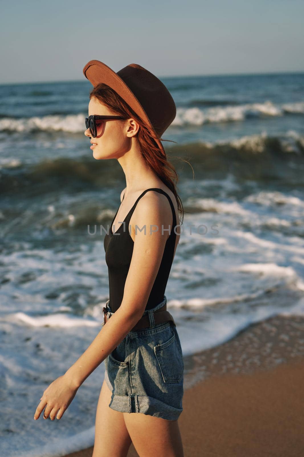 cheerful woman in sunglasses and a hat walks along the ocean. High quality photo