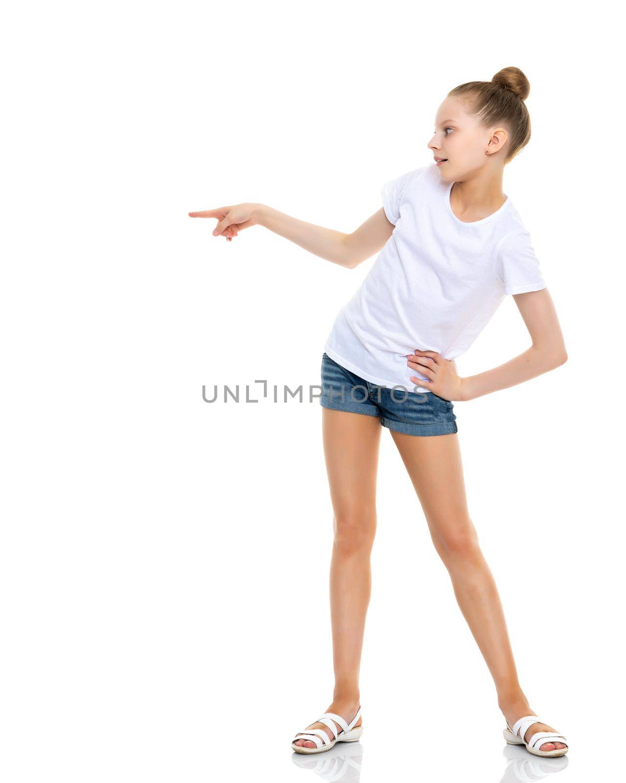 A nice little girl in a clean white T-shirt is pointing at something. The concept can be used to advertise goods and services whose logo can be printed on the surface of a shirt. Isolated on white background.
