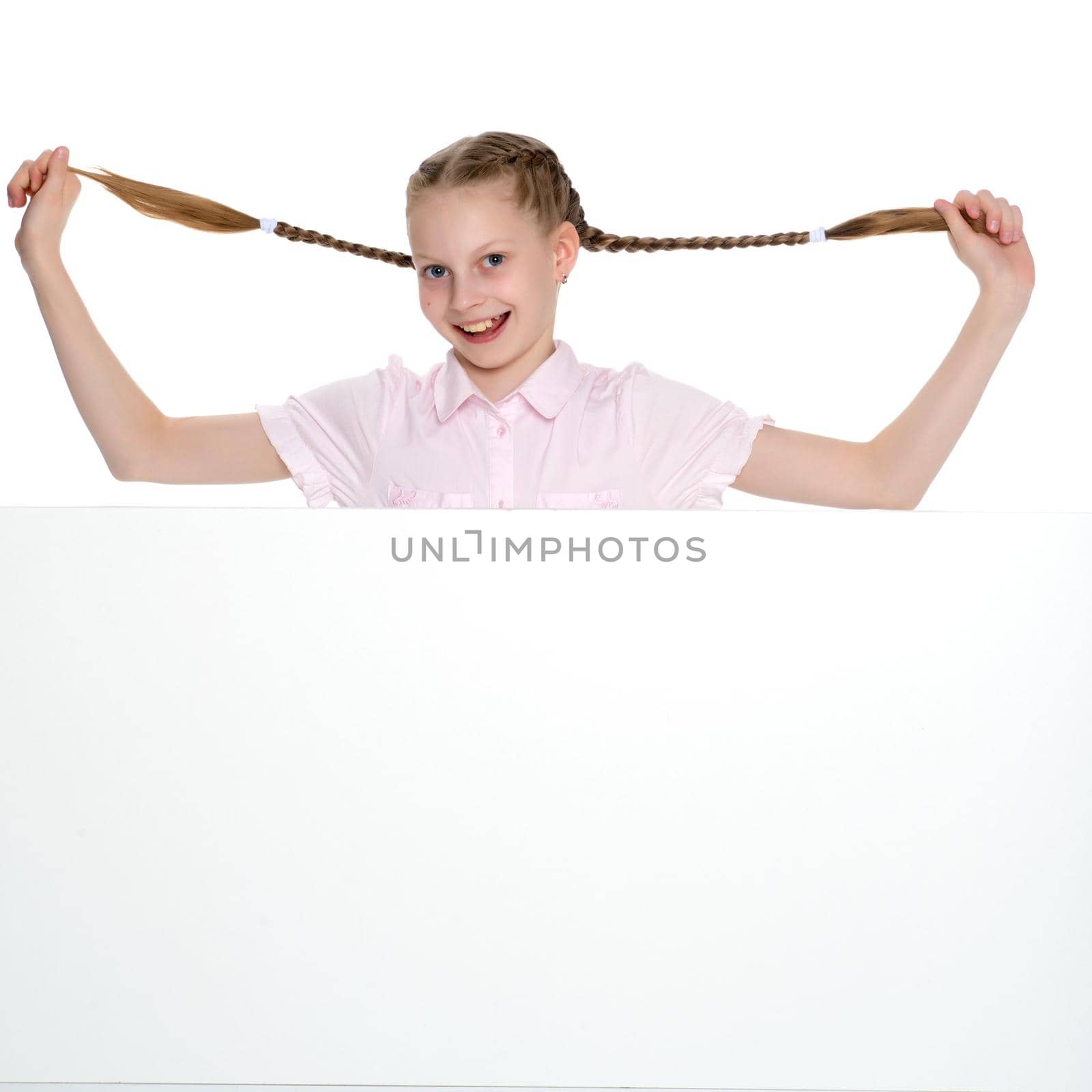 A beautiful little girl is pulling herself in pigtails. The concept of education, advertising, children's emotions. Isolated on white background.