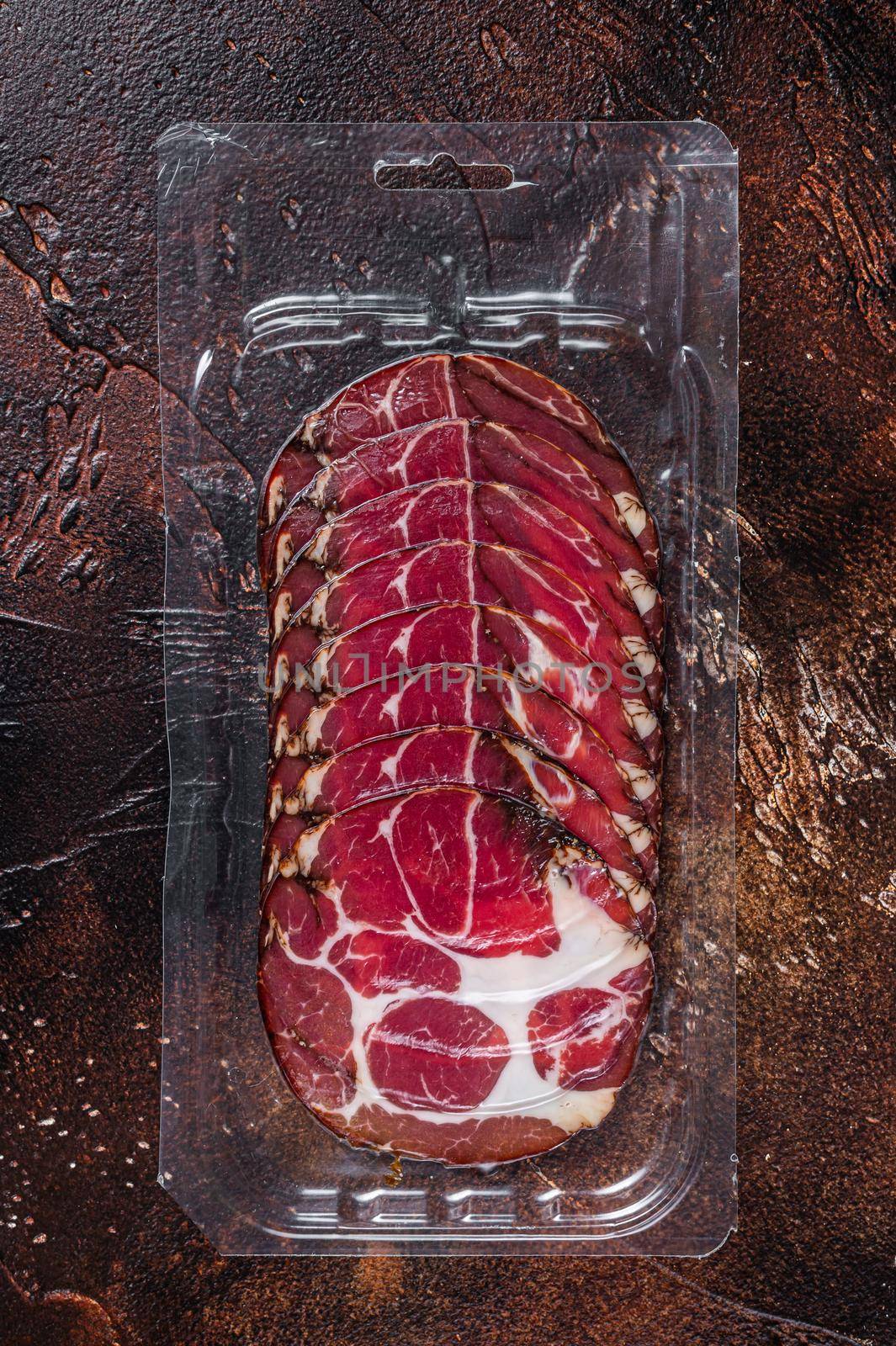 Italian sliced cured coppa meat in vacuum packaging. Dark background. Top view.