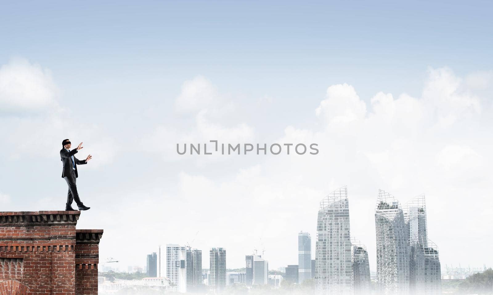 Businessman with blindfolder on eyes walking on building top