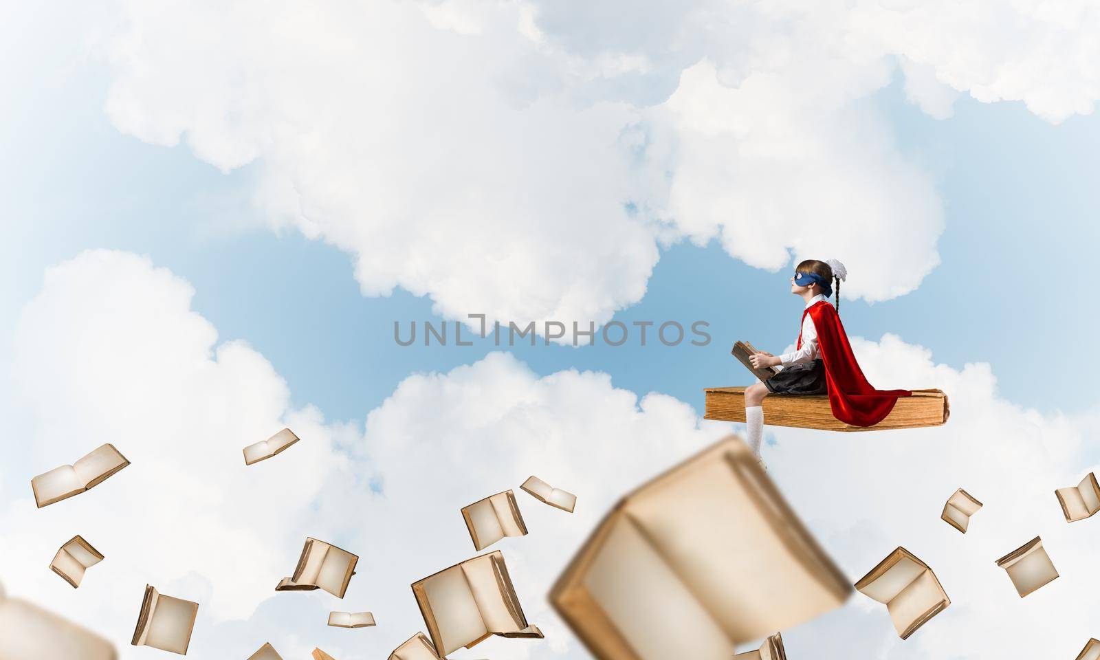 Little child in mask and cape floating on book in sky and reading