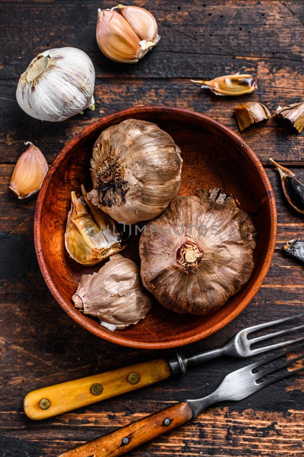 Bulbs and cloves of fermented black garlic in a plate. Dark wooden background. Top view.