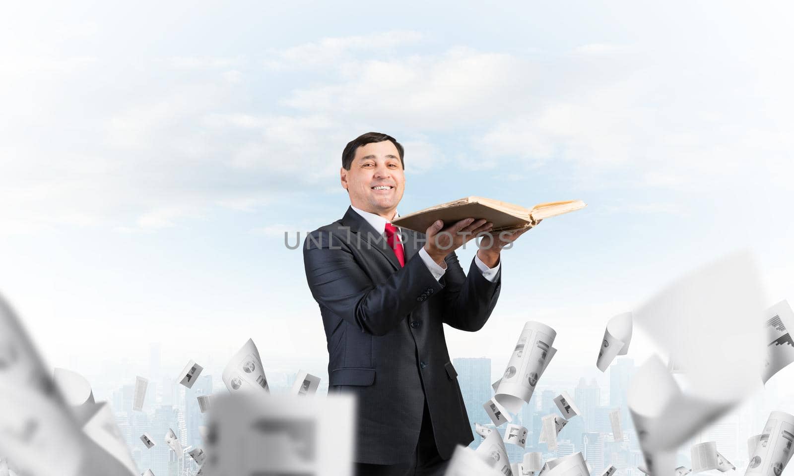 Happy businessman holding old open book. Smiling man in suit standing on downtown background with falling paper documents. Lawyer holding legal regulation book. Business accounting and consulting