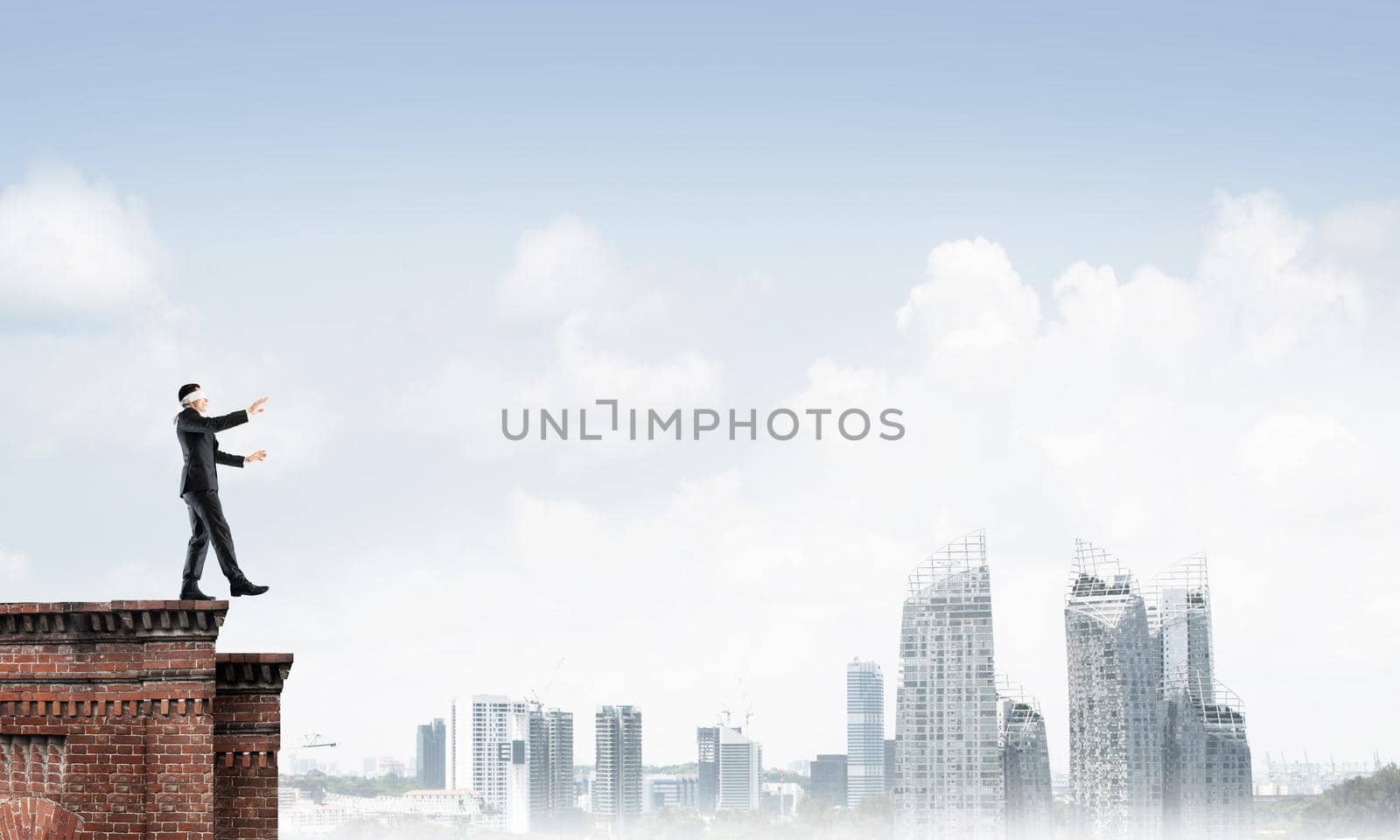 Businessman with blindfolder on eyes walking on building top