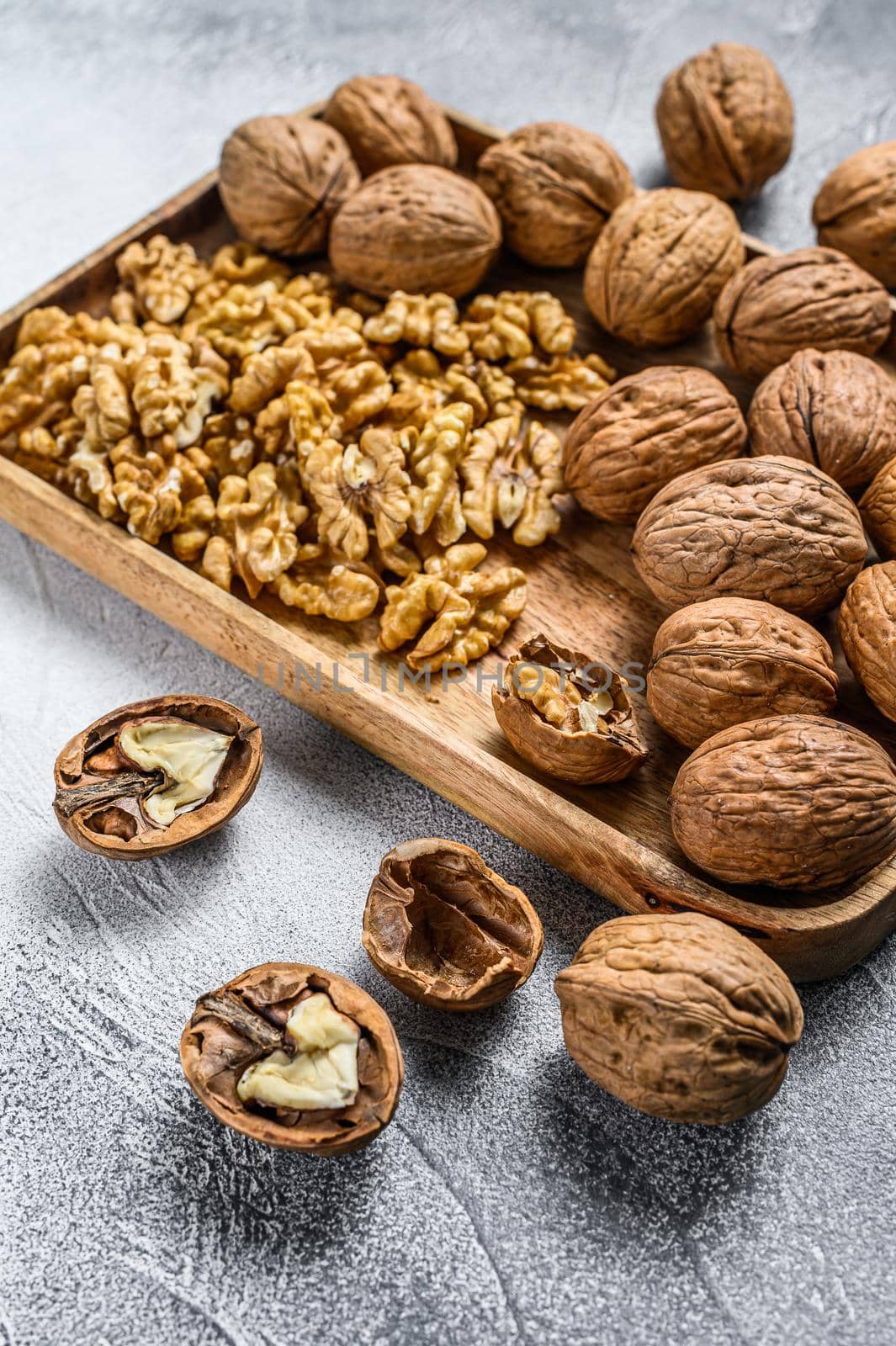 Walnuts in a wooden plate and walnut kernels. Gray background. Top view.