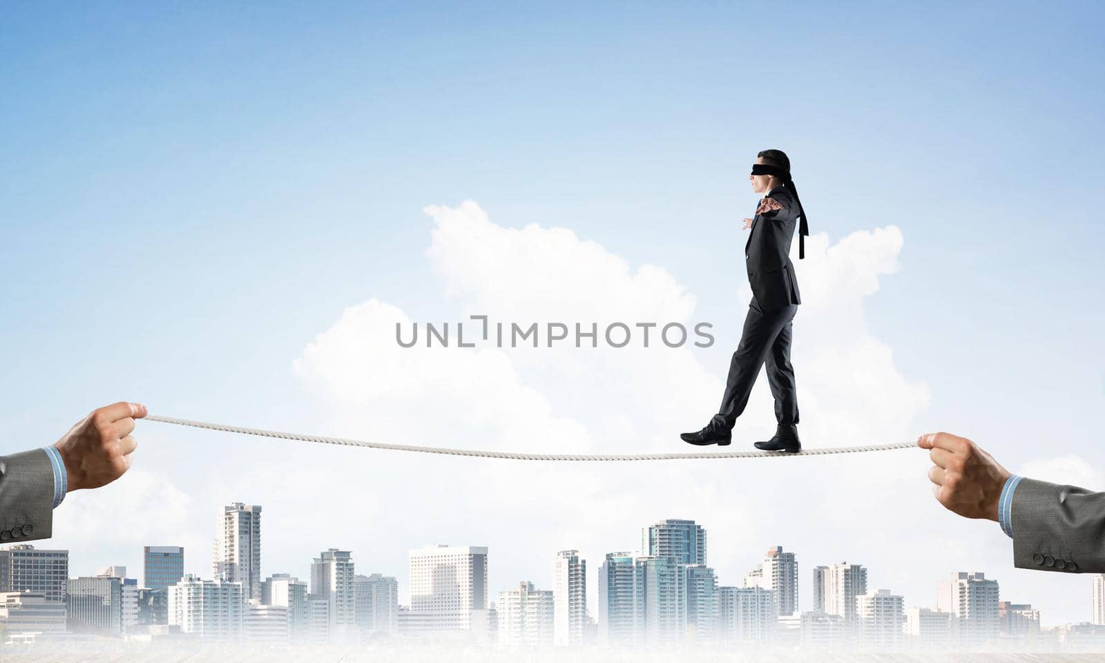 Businessman with blindfolder on eyes walking on rope over cityscape background