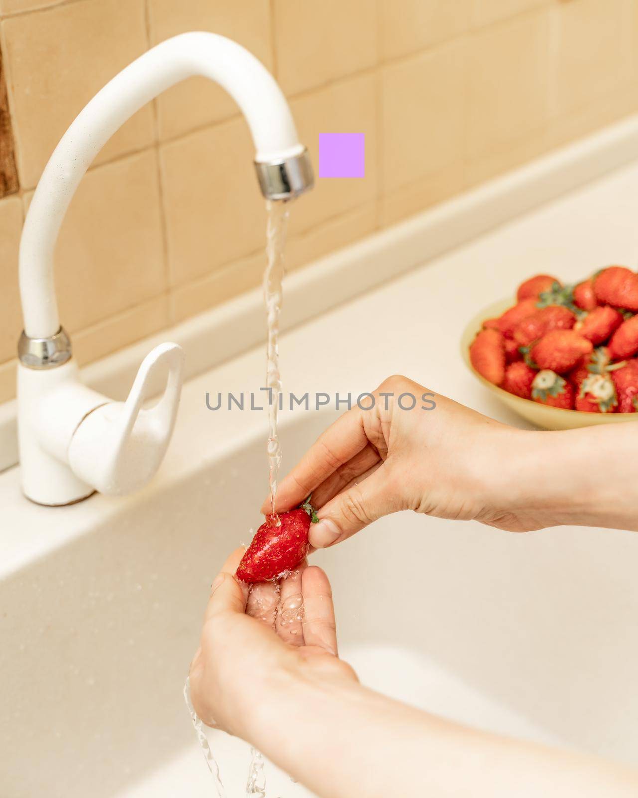 Women's hands wash strawberries and blueberries under a stream of water in the kitchen sink. Selective focus. Wash fruit before eating by Matiunina