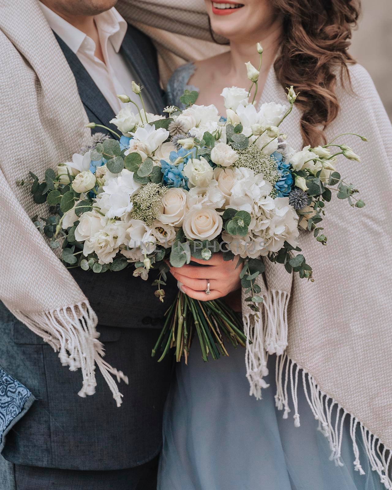 the couple is embracing holding a beautiful bouquet of flowers, the girl is wearing a blue long dress, the man is wearing a suit and a plaid is thrown over. wedding concept by Matiunina