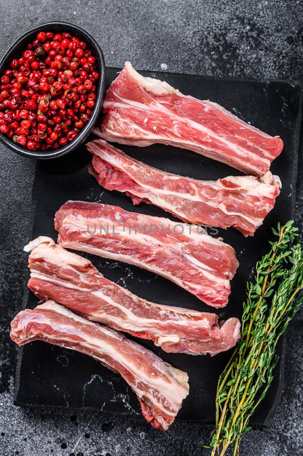 Raw sliced veal short spare loin ribs on a marble board. Black background. Top view. Copy space.