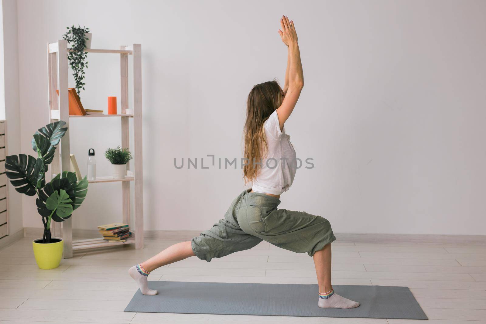 Woman practise yoga performs. Pose on mat inside of cozy room with plants and greenery. Healthy lifestyle