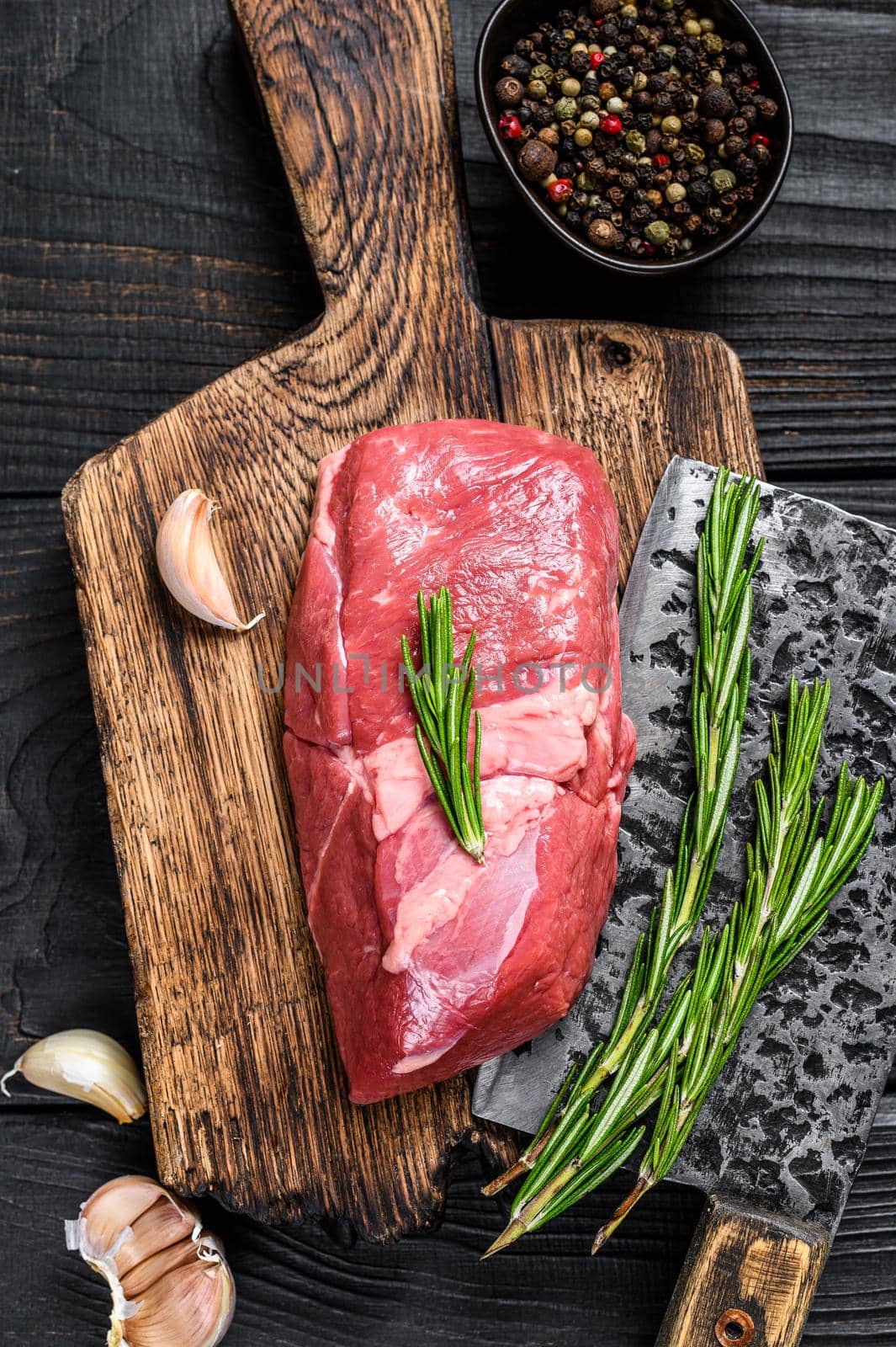 Raw lamb meat sirloin steak on a wooden cutting board. Black wooden background. Top view by Composter